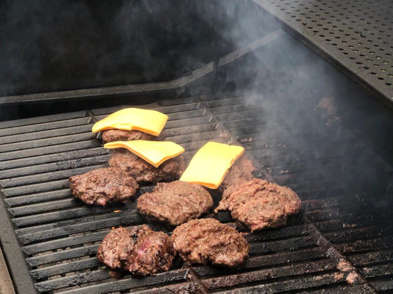 A grill with some hamburgers and cheese on it